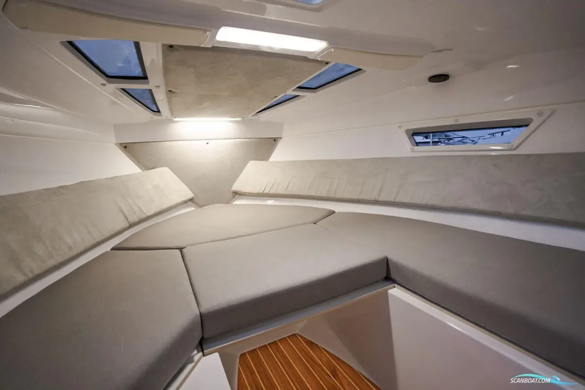 Interior of a modern boat cabin with grey cushions, wooden flooring, and overhead windows for natural light.